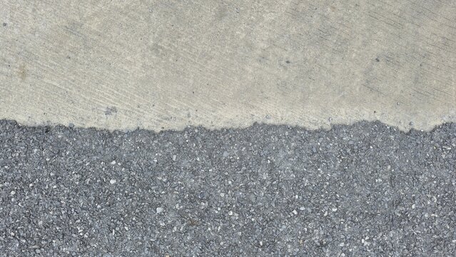 Asphalt and concrete road surface texture contrast. Top view of the junction between asphalt and concrete ground. Border line between grey cement wall and asphalt road.