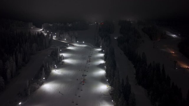 Remote Aerial View Capturing Night Maintenance On Ski Slopes With Machinery And Surrounding Trees