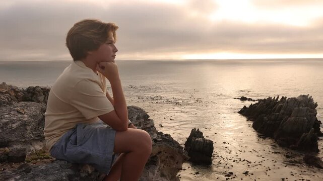 young boy looking at incoming fog meeting rocky coastline at sunset, DeKelders, South Africa