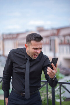 Angry businessman screaming at smartphone screen outdoor with copy space