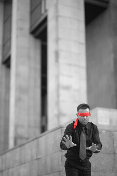 Blindfolded businessman searching way in black and white city with copy space