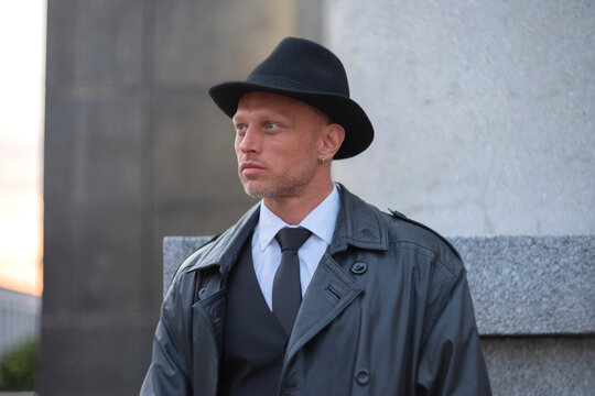 Serious man in trench coat and fedora hat looking away with copy space