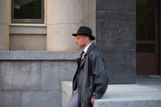 Confident spy agent in leather coat sitting near granite columns with copy space