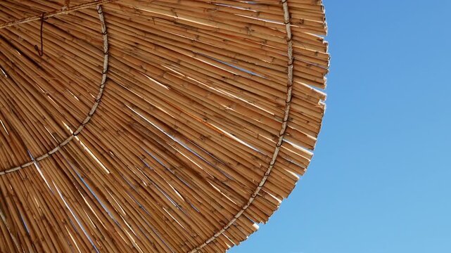Bamboo parasol against bright blue sky, tropical beach resort atmosphere, sunny summer holiday destination.