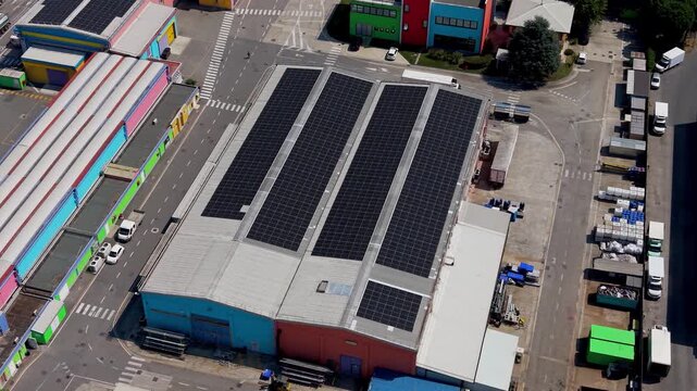 Rooftop Solar Power: Aerial view of a large industrial building with rows of solar panels installed on its roof, representing renewable energy and sustainable infrastructure.