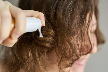 Fototapeta premium Woman Applying Conditioner To Damp Curly Brown Hair With Pump Bottle In Closeup Indoor Setting Showing Hand Profile And Smile During Personal Grooming Routine.