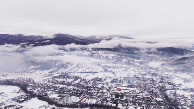 Frozen Town Beneath Cloudy Skies. Aerial Perspective Of Snowdusted Urban Area Surrounded By Mountains