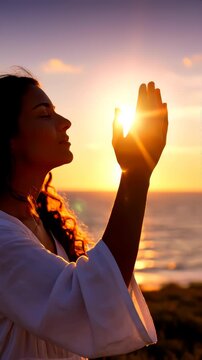 A praying woman stretches out her hand to the sun against the sunset, asking for God's blessing. Vertical video, shorts.