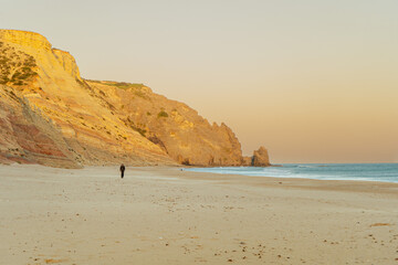 Golden hour sunset over the Atlantic Ocean shoreline with rolling hills, warm light reflecting on the water and a scenic coastal landscape with man walking. © Vaidile