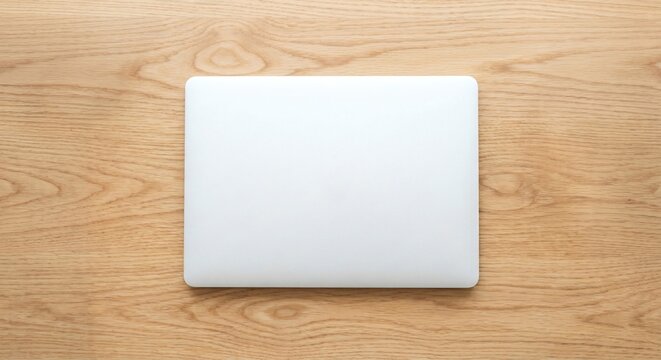 Blank white closed laptop computer mockup flat lay on wooden desk