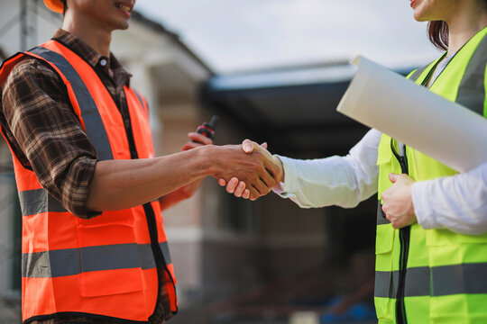 Builders wearing safety vests shaking hands on a construction site, symbolizing partnership, teamwork, and a successful deal