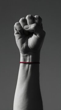 Monochrome raised fist with red string bracelet. Symbol of protest struggle solidarity hope. Powerful gesture conveys strength unity resistance against oppression injustice social change.