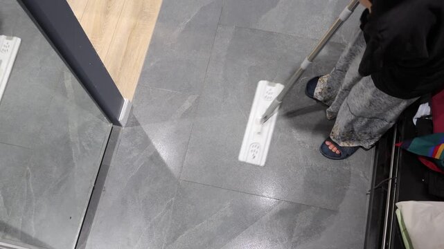 A flat mop cleans gray tile at the threshold between the entryway and a light wooden floor.