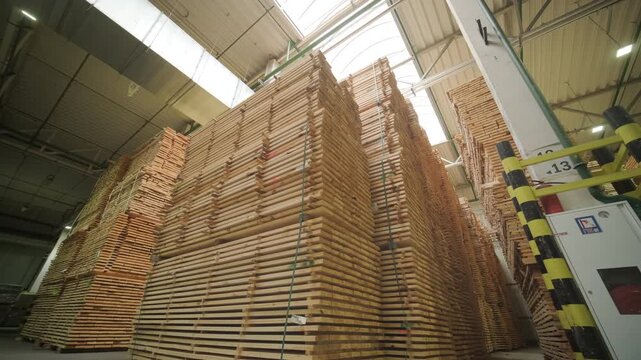 A large industrial warehouse featuring a forklift operating among stacks of dried wooden planks prepared for further furniture or flooring production