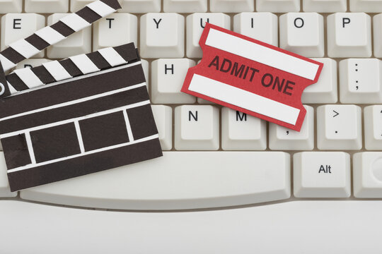 Movie clapper and ticket on a white computer keyboard for online streaming