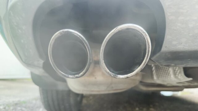 The dual chrome tailpipes release a faint stream of vapor into the open air. This idling engine process generates a low, consistent rumble and a soft whooshing sound.