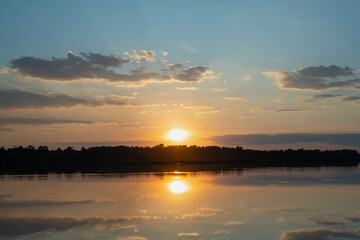Obraz premium Sunset sky over calm river with golden reflection and dark tree line at horizon, peaceful evening landscape