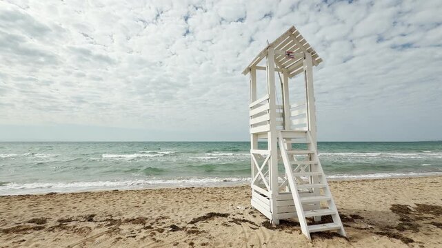A tall wooden rescue tower stands watch over the restless sea and sandy shore. The wide sky and rolling waves create a vast, breezy feeling of coastal freedom and quiet anticipation.