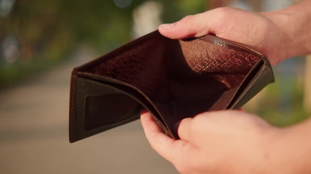 Close-up of a person holding open an empty leather wallet with no cash inside. Empty wallet, concept of financial crisis. Man showing an empty wallet with no money or credit cards inside. 
