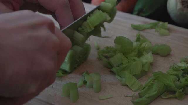 Close-up footage of fresh celery being chopped on a wooden cutting board in a kitchen. Cinematic food preparation scene with natural lighting and detailed hand movement.