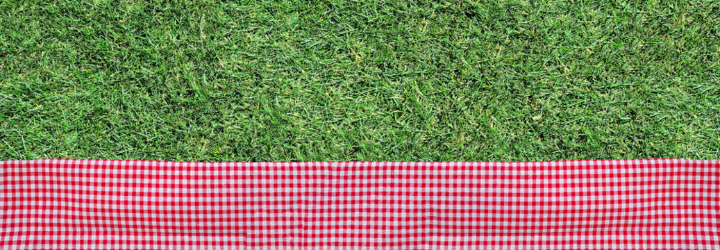 Picnic theme grass background with red and white check cloth bottom border. Top view banner. Copy space.