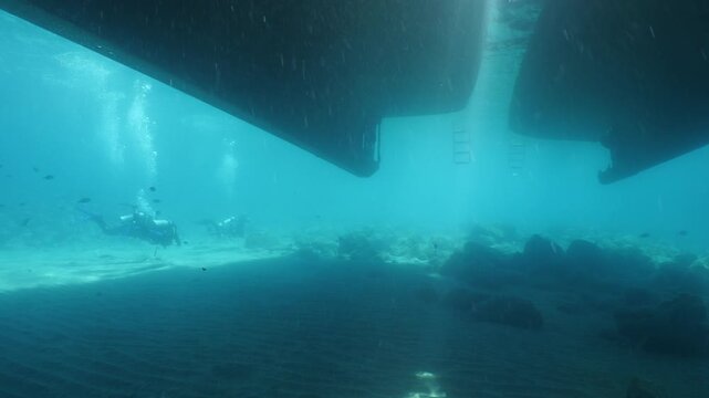 scuba diver scenery under the parked boats with sun beams and rays underwater