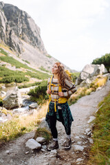 Female hiker with yellow backpack walks along mountain trail alongside stream. Woman enjoys  mountain scenery and feels a sense of freedom. Concepts of adventure, hiking, and sports. © maxbelchenko