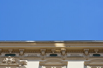 Low angle view of a decorative historic building facade with detailed plaster stucco ornaments and a roof cornice under a clear blue sky. © nahhan