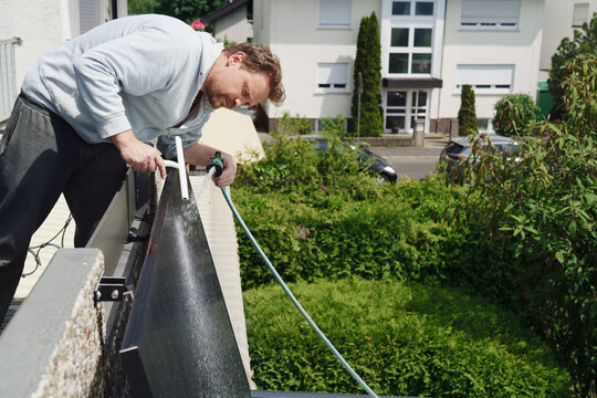A man cleaning solar panels on a home balcony power plant on a sunny day.
