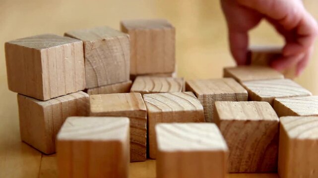 Natural wooden blocks for construction, pile of square timber cubes on table, child hand playing with wood building blocks for education