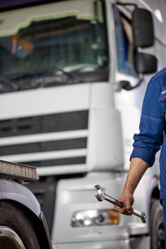 A skilled mechanic in blue overalls confidently holds a wrench, symbolizing expertise in quality truck repairs. The image captures dedication and professionalism in automotive maintenance.