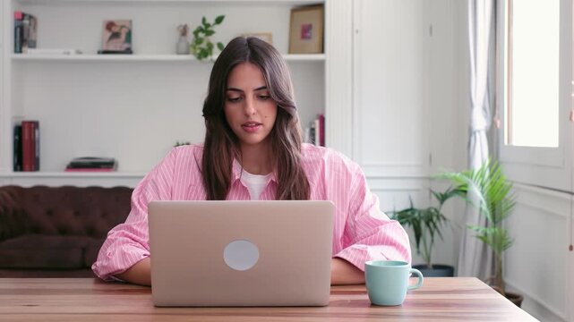 Young businesswoman closing her laptop after finishing work at home, feeling tired and bored while sitting at her desk in the living room, showing signs of exhaustion and overwork