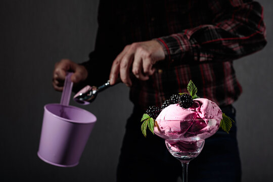 Man puts blackberry ice cream in a sundae cup.