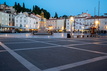 Obraz premium Tartini Square in Piran, Slovenia at Blue Hour with Historic Venetian Architecture and Illuminated Cafes Surrounding the Famous Monument. Evening Scene in the Heart of the Adriatic Coastal Town