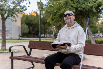 Fototapeta premium Blind Man With Cane Sitting Reading in Braille in a Park