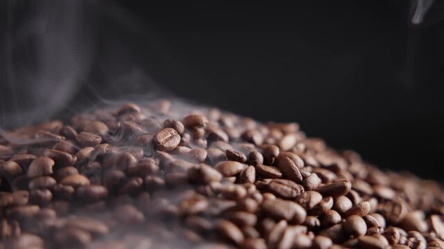 Slow motion steaming coffee beans heaped on dark studio tabletop with rising smoke and drifting wisps.