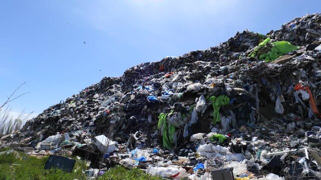 Workers collect trash near a large mound of garbage at an abandoned dump in an area filled with pollution and waste materials