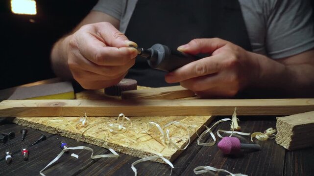 Skilled craftsman prepares a wood piece using a rotary tool, showcasing detailed hand movements and various tools on a wooden workbench