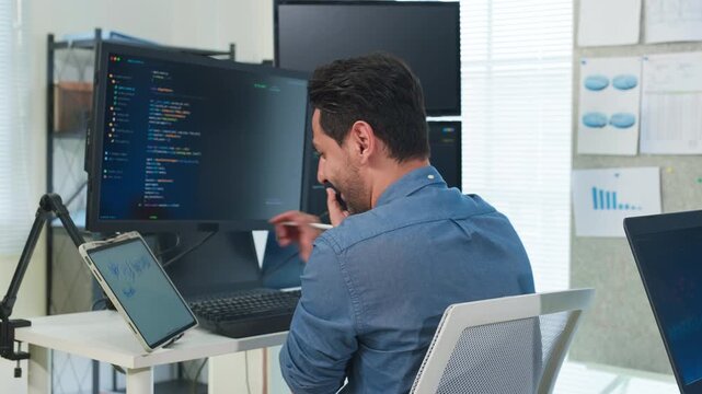 Two focused software engineers collaborating on code in modern office, professional developers discussing project on laptop and computer screen