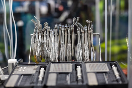 Stainless Steel Dental Extraction Instruments Display. Close-up of shiny stainless steel dental extraction tools arranged on a rack with surgical instrument kits in the foreground.