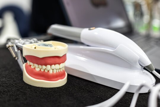 Dental Teeth Model with Digital Scanner. Close-up of a dental teeth model beside a digital scanner handpiece and equipment in a modern clinic setting.
