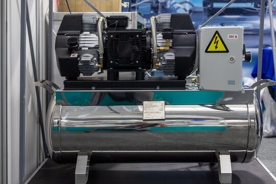 Stainless Steel Industrial Air Compressor Unit. Front view of a stainless steel air compressor with motor, control box, warning sign, and polished pressure tank.