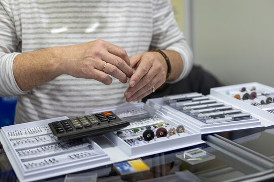 Customer Choosing Dental Supplies at Counter. Close-up of a customer examining small dental accessories and tools beside a calculator at a clinic or supply store counter.