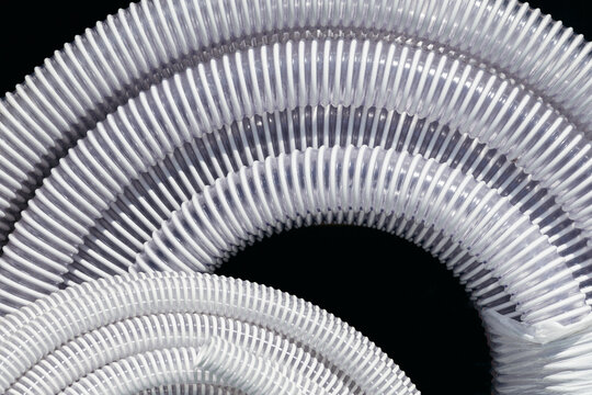 White corrugated plastic pipes neatly coiled against a solid black background.