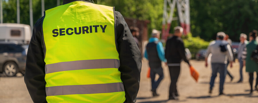 Security guard in high-visibility vest monitoring crowd at outdoor public event, safety and crowd control concept