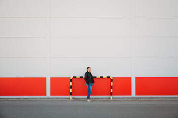 A casually dressed woman stands against a bold red and white industrial wall, conveying urban minimalism, contrast, solitude and contemporary street style. © Bits and Splits