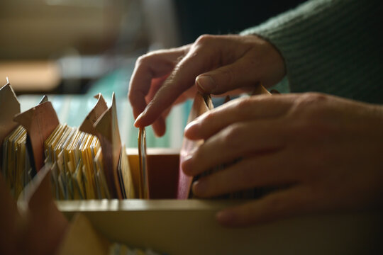 Close-up of female hands browsing old card catalog drawers, vintage library research concept