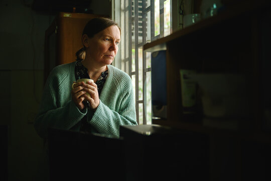 Female librarian standing by window in old library office, drinking coffee in quiet reflective moment