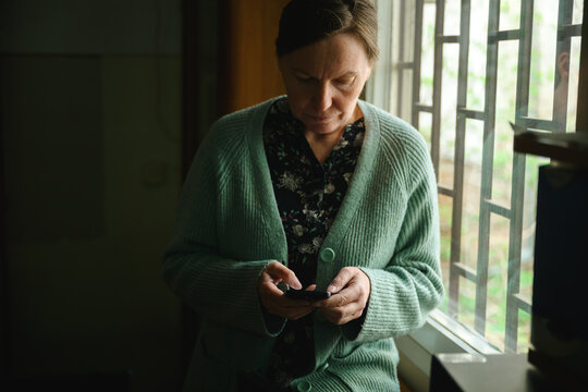 Woman checking mobile phone in vintage library workspace, soft daylight and calm reflective atmosphere, browsing internet in quiet moment