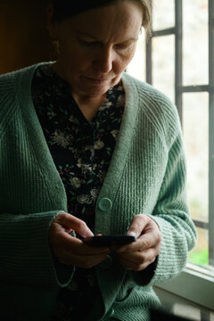Woman using smartphone in old office library workspace, soft daylight and calm reflective atmosphere, browsing internet in quiet moment